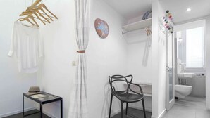 A modern bathroom with a shower, toilet, and sink. There is a chair and a table with a hat on it.