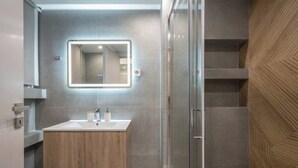 A modern bathroom with a wooden vanity, a glass shower enclosure, and a mirrored wall. - Home in Athens (Kallithea)