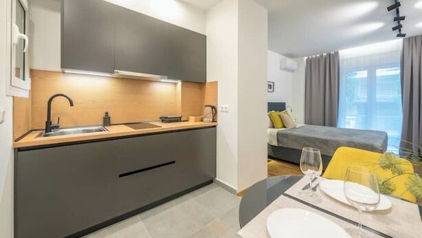 A modern kitchen with a built-in stove, a sink, and a dining area with a table set for two. - Home in Athens (Kallithea)