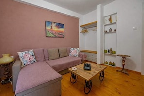 A living room with a pink sofa, a wooden coffee table, a decorative table, and a wall-mounted shelf with items.