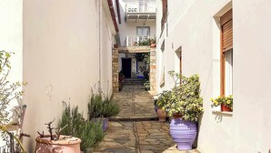A narrow stone-paved alleyway with potted plants on either side, leading to a building entrance. - Dinas Apartment Alonissos - Nefeli Summer Haven (Patitiri)