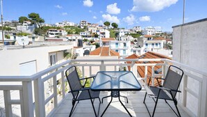 A balcony with two chairs and a table, overlooking a residential area with terracotta roofs and white buildings. - Dinas Apartment Alonissos - Nefeli Summer Haven (Patitiri)