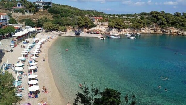 A beach with clear turquoise water, a row of sun umbrellas, and a few people swimming. - Dinas Apartment Alonissos - Nefeli Summer Haven (Patitiri)