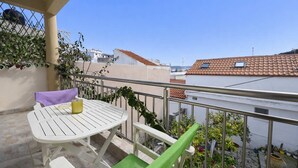 Ein Balkon mit einem weißen Tisch und Stühlen, einem gelben Getränk und Topfpflanzen.