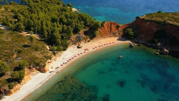 An aerial view of a coastal area with a sandy beach, clear turquoise waters, and a forested hillside. - Flower's Studio Alonnisos - Artemis Summer Escape (Patitiri)