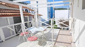 A covered outdoor area with a table and chairs, a hanging swing, and a view of buildings in the background. - Flower's Studio Alonnisos - Artemis Summer Escape (Patitiri)