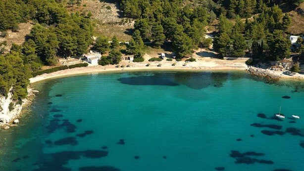 Vista aérea de una zona costera con un mar turquesa cristalino, una playa de arena y edificios dispersos.