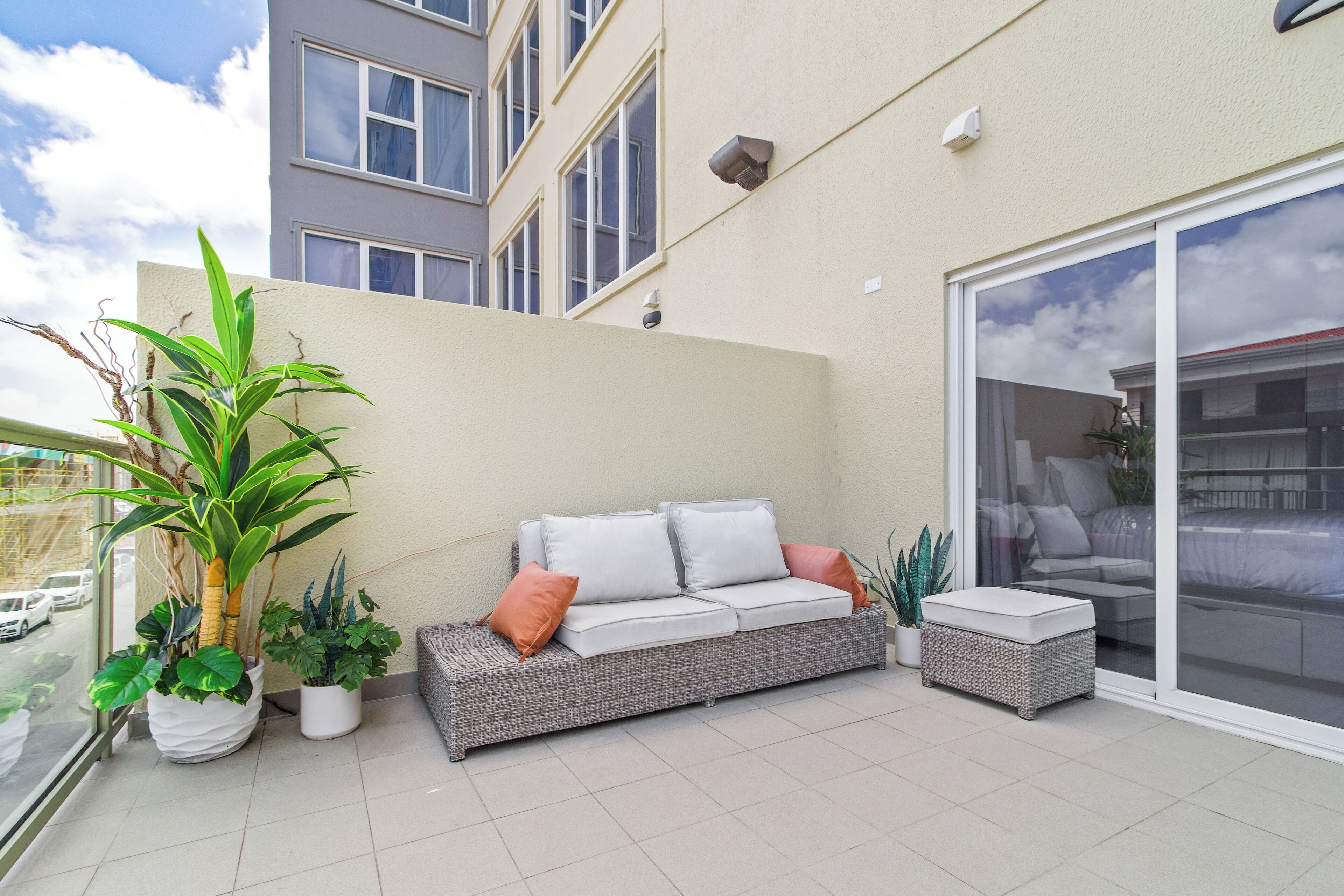 Ein Balkon mit einem Korbsessel, zwei Topfpflanzen und einer Schiebetür, die auf einen Balkon mit einem Bett führt.