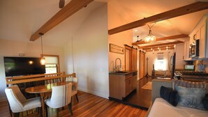 A modern living room with a wooden dining table, two chairs, a sofa, a kitchen area with a sink and stove, and a television.