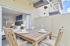 Una mesa de madera para comer con platos blancos y vasos, frente a una pared color beige con un balcón.