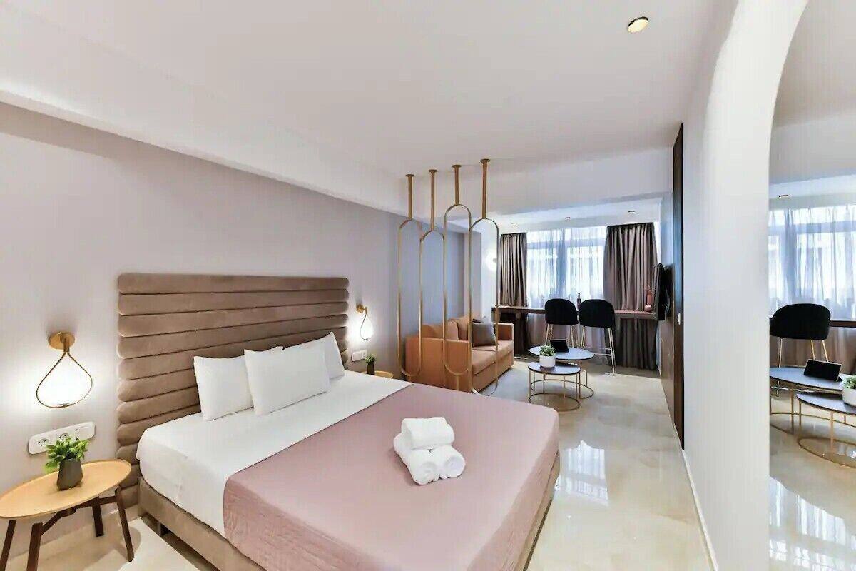 Une chambre d’hôtel moderne dotée d’un grand lit, d’un coin salon avec un canapé et des fauteuils, d’une petite table avec une plante et d’un téléviseur.