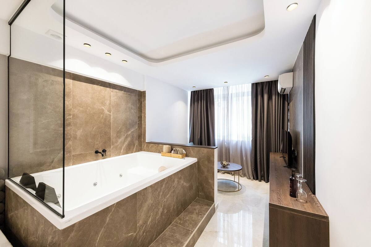 Une salle de bain moderne avec une grande baignoire, un meuble-lavabo avec un miroir et une petite table ronde.