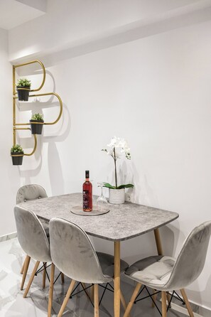 Et spiseområde med et marmorbord, fire grå polstrede stole, en guldfarvet metalkasse med plantepotte, en vinflaske og en hvid orkidé.