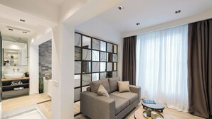 Una sala de estar moderna con un sofá gris, una mesita redonda con una bandeja y un ventanal con cortinas.