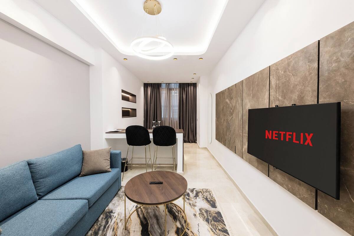 Un salon moderne avec un canapé bleu, une table basse et un grand téléviseur à écran plat affichant le logo de Netflix.