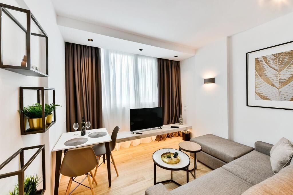 A modern living room with a sofa, a dining table with chairs, a TV, and a small coffee table.