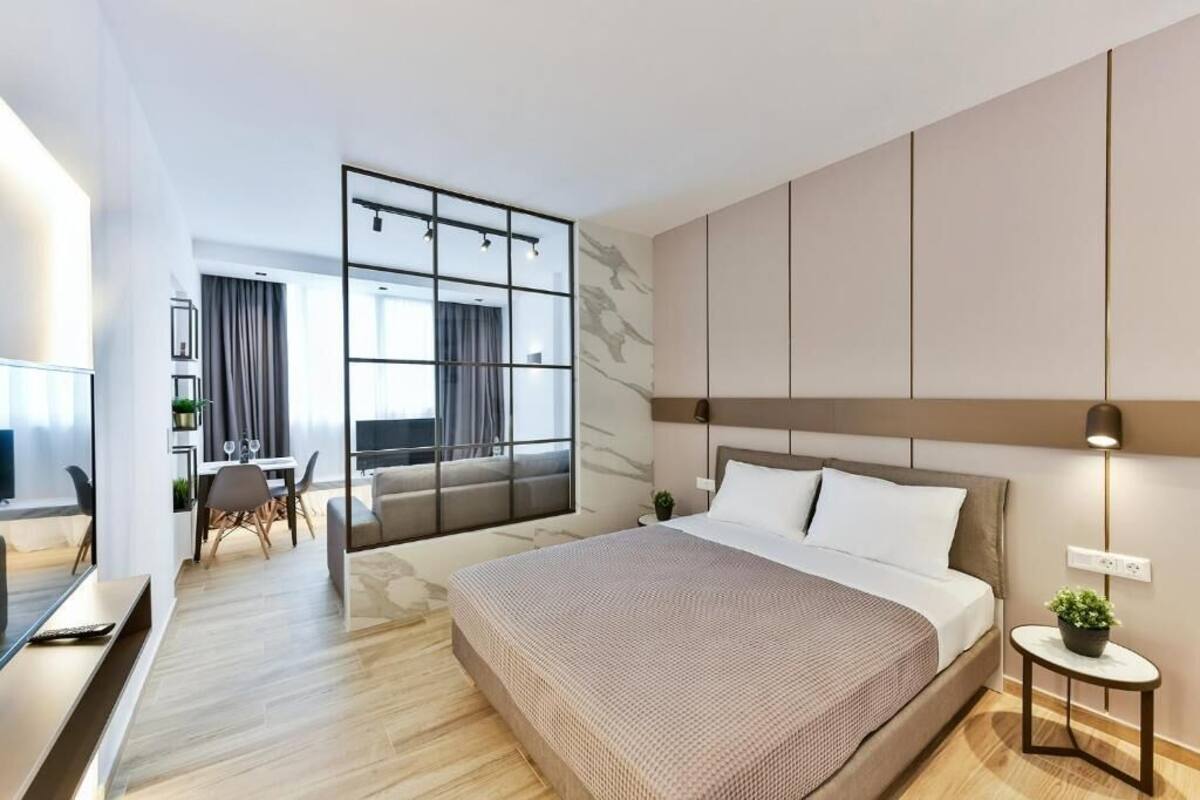 Une chambre d’hôtel moderne dotée d’un grand lit, d’un coin salon avec une table et des chaises, et offrant une vue sur la ville grâce à de grandes fenêtres.