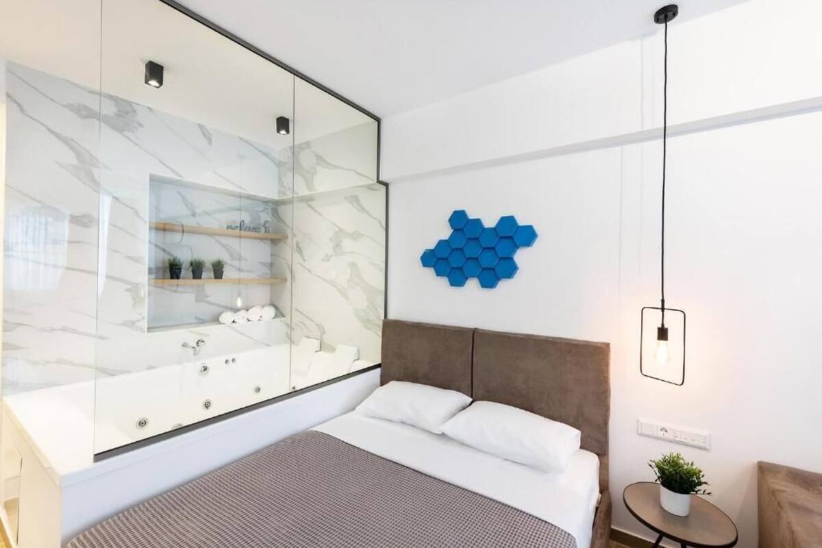 Une chambre moderne dotée d’une douche en verre, d’un lit avec du linge de lit blanc, d’une tête de lit marron et d’une décoration murale hexagonale bleue.