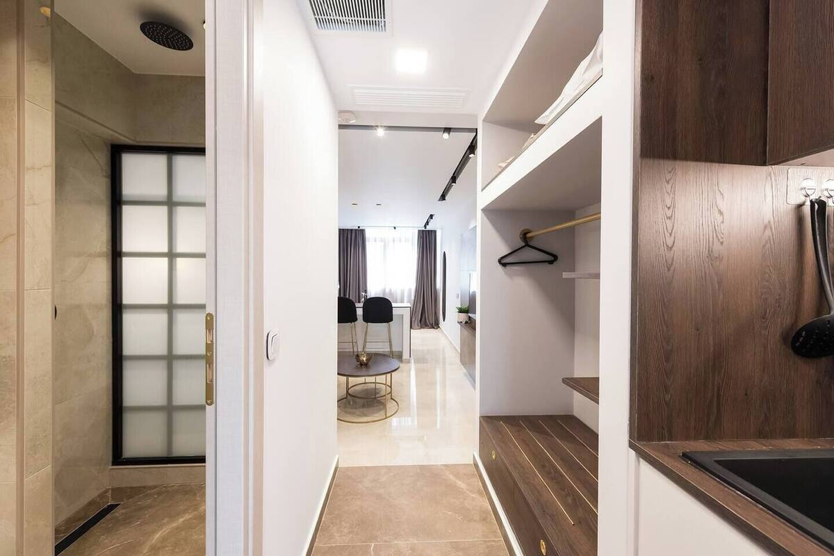 Une chambre d’hôtel moderne dotée d’une porte coulissante, d’un coin repas avec une table et des chaises, et d’une coiffeuse en bois avec un lavabo.