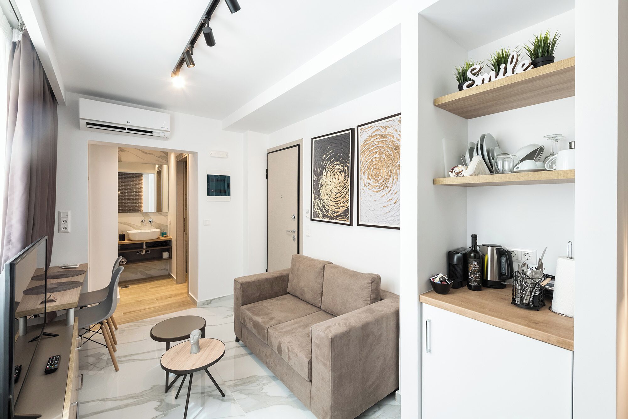 A modern living room with a sofa, a coffee table, and a dining area with a table and chairs. There is a kitchen area with a countertop and shelves.