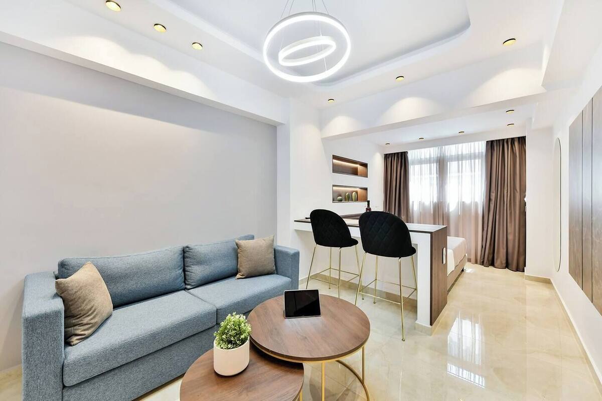 Un salon moderne avec un canapé, une petite table sur laquelle est posée une plante, et un ordinateur portable. On y trouve également un coin repas avec un comptoir de bar et des chaises.