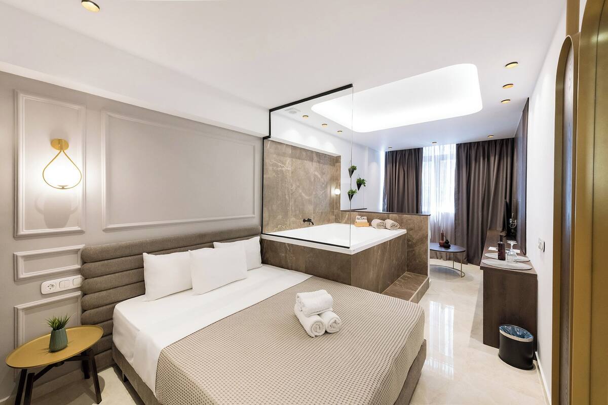 Une chambre d’hôtel moderne avec un grand lit, une salle de bain avec baignoire et une petite table agrémentée d’une plante.