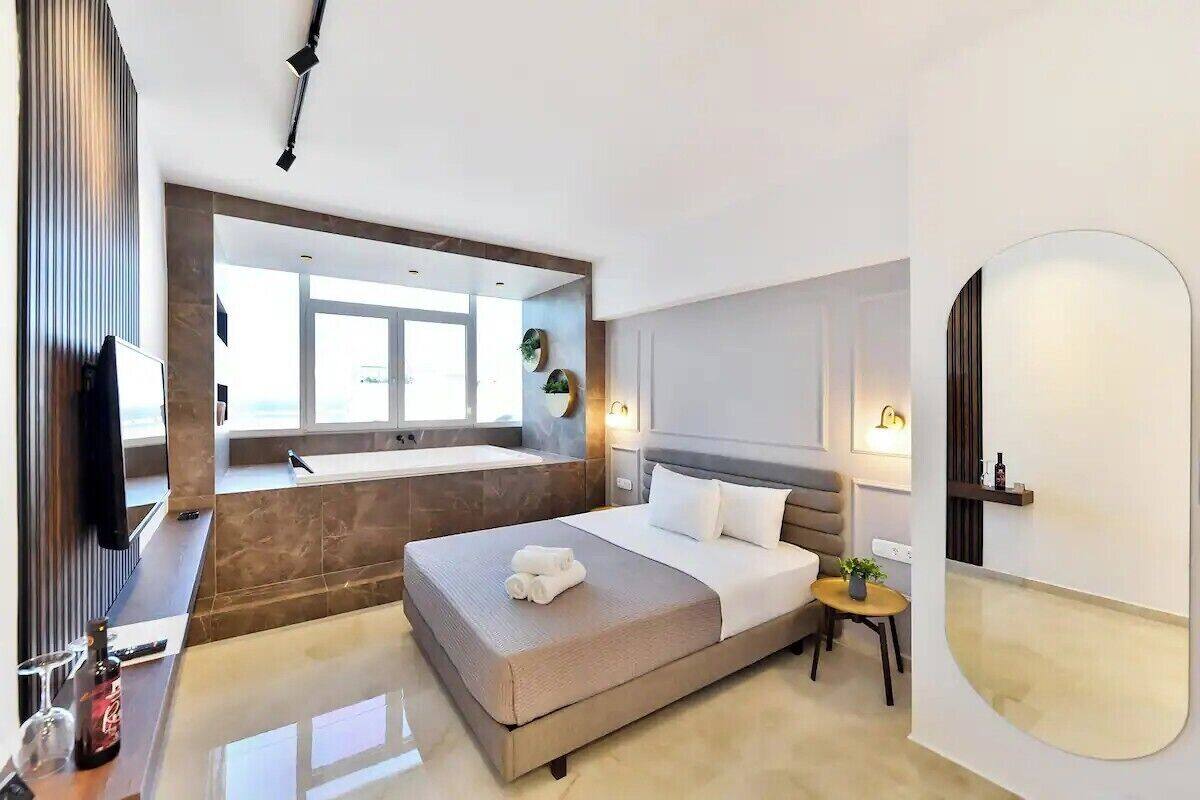 Une chambre d’hôtel moderne, dotée d’un grand lit, d’une petite table, d’un miroir et offrant une vue sur l’extérieur.