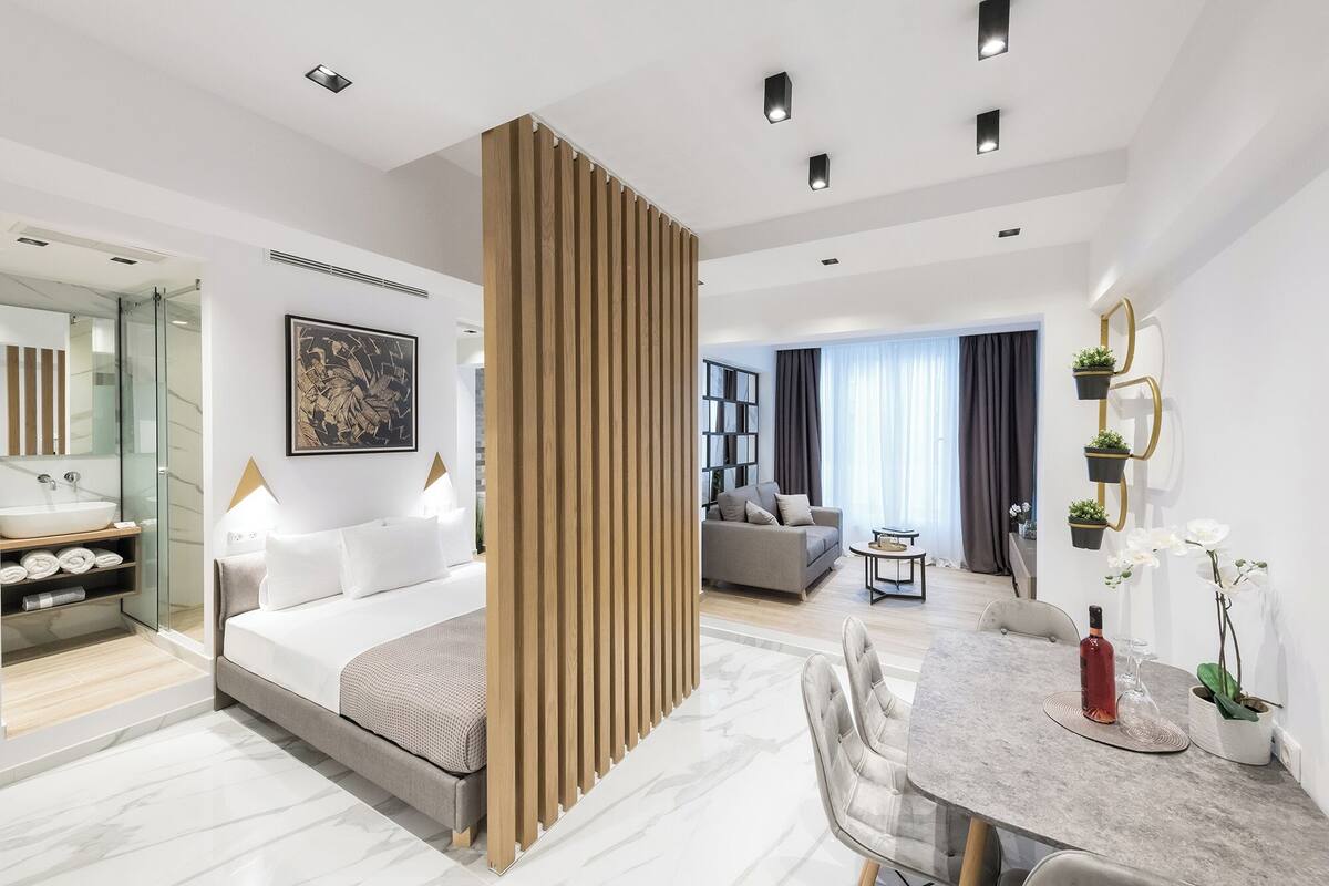 Une chambre d’hôtel moderne comprenant un lit, un coin repas, une salle de bain avec un grand miroir et un espace salon avec un canapé et une table basse.