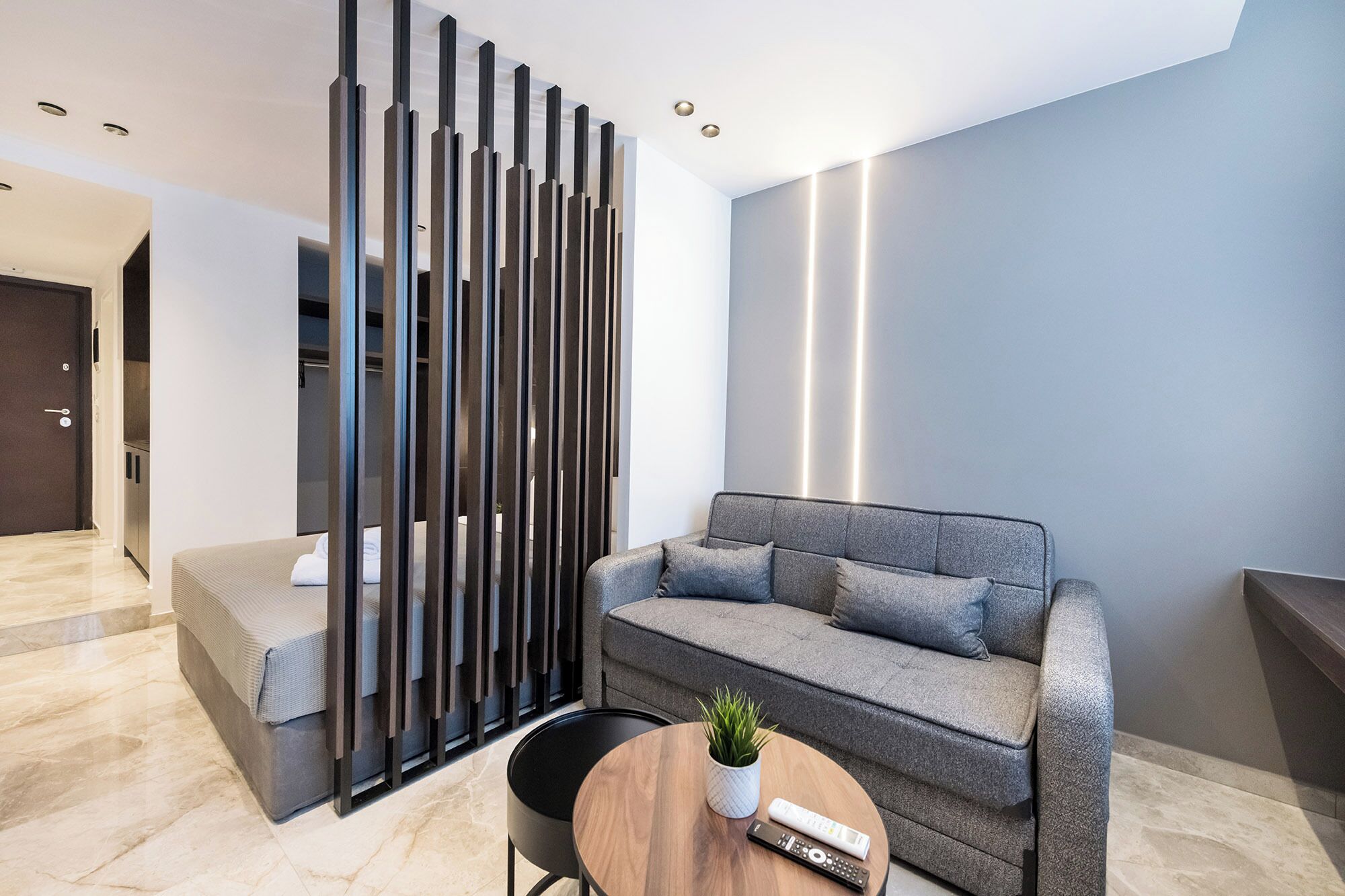 A modern living room with a grey sofa, a wooden coffee table, and a decorative panel with vertical slats.