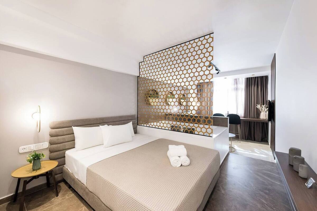 Une chambre d’hôtel moderne avec un grand lit, une petite table d’appoint agrémentée d’une plante, un panneau décoratif au mur et une vue sur la salle de bain.