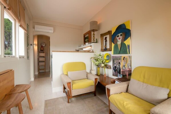 A living room with a yellow sofa, a yellow armchair, and a wooden coffee table. There is a painting on the wall and a window with curtains. - Cocoon with balcony - sea view (Sainte-Maxime)