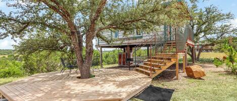 A wooden deck with a staircase leading to a house surrounded by trees.