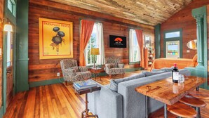 Ein gemütlicher Holzraum mit gemusterten Sesseln, einer Couch und einem Holztisch mit einer Weinflasche.