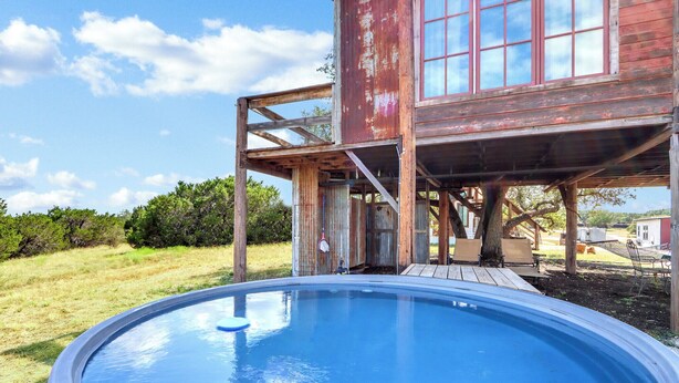A rustic wooden structure with a swimming pool in the foreground. - Romantic Treehouse Escape in Hill Country (Lampasas)