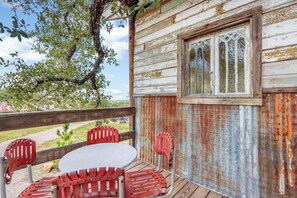 Una cabana rústica de fusta amb una taula rodona i cadires vermelles, una finestra amb vitralls i vista a una zona enjardinada.