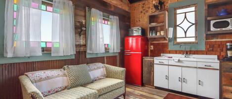 A cozy room with a wooden ceiling, a red refrigerator, a white sink, and a patterned sofa.