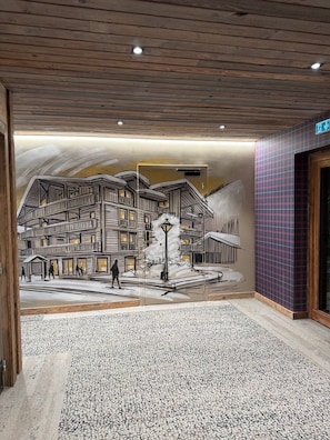Un corridoio con pavimento decorato e un murale raffigurante un edificio con balconi e persone.