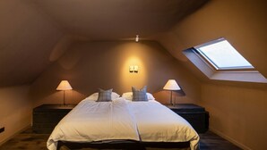 Un dormitorio con una cama grande, dos mesitas de noche con lámparas, un tragaluz y un aplique de pared.