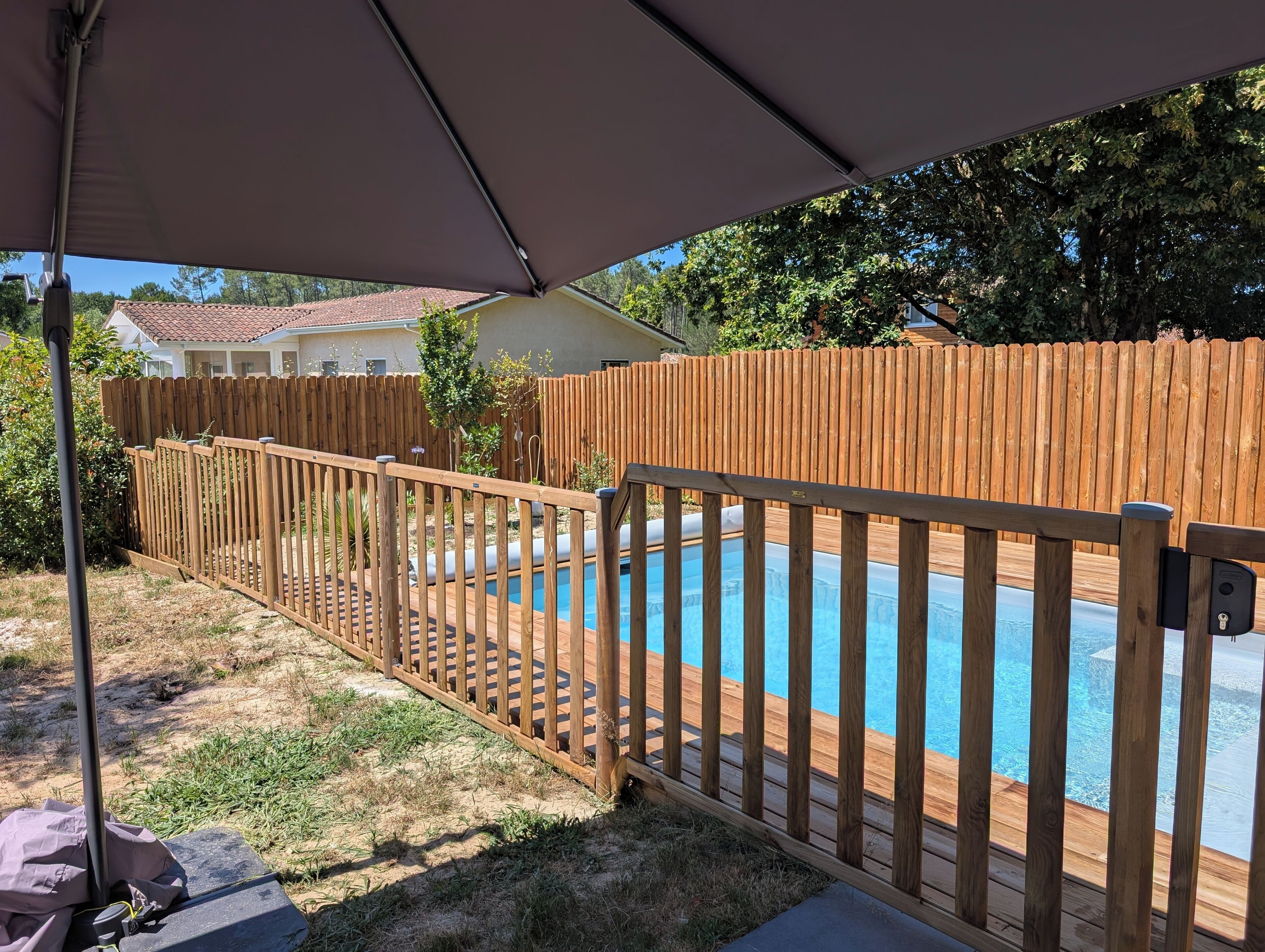 A backyard with a wooden pool surrounded by a wooden fence and a covered patio area.