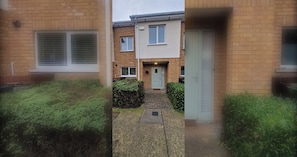 Een woonhuis met een gevel van baksteen, een voordeur en een kleine voortuin met hagen.