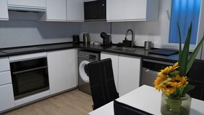 Eine moderne Küche mit weißen Schränken, einer schwarzen Arbeitsplatte, einem eingebauten Backofen, einer Waschmaschine und einem Spülbecken. Auf der Arbeitsplatte steht eine Vase mit Blumen.