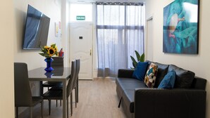 Ein Zimmer mit Esstisch, Stühlen, einer Couch, einem Fernseher und einem Gemälde.