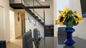 Ein moderner Essbereich mit einem Glastisch, schwarzen Stühlen und einer blauen Vase mit Sonnenblumen.