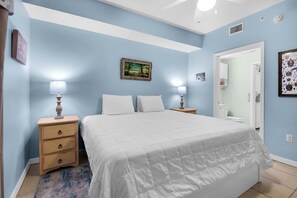 A bedroom with a bed, two bedside tables, a nightstand, a rug, a painting, and a door leading to another room. - 🏝️Hooked on the Beach: Beachfront Condo Near Pier, Great Amenities🏝️ (Navarre Beach)