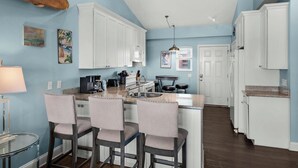 A kitchen with white cabinets, a bar area with three chairs, and a dining table.