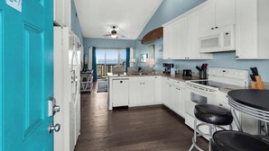 A kitchen with white cabinets, a microwave, and a stove. There is a blue door with a label, a ceiling fan, and a window with a view.