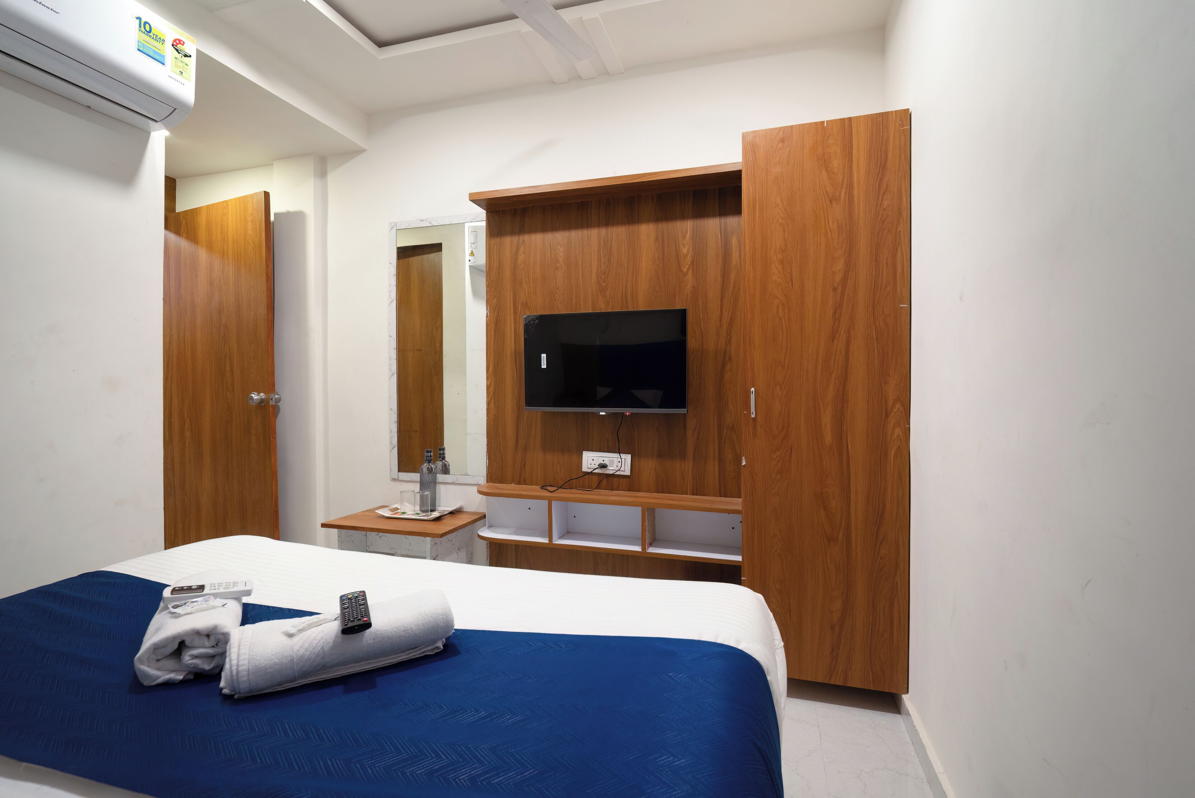 Et hotelværelse med en seng, et fjernsyn ophængt på et træskab, et lille bord med et spejl og en aircondition.