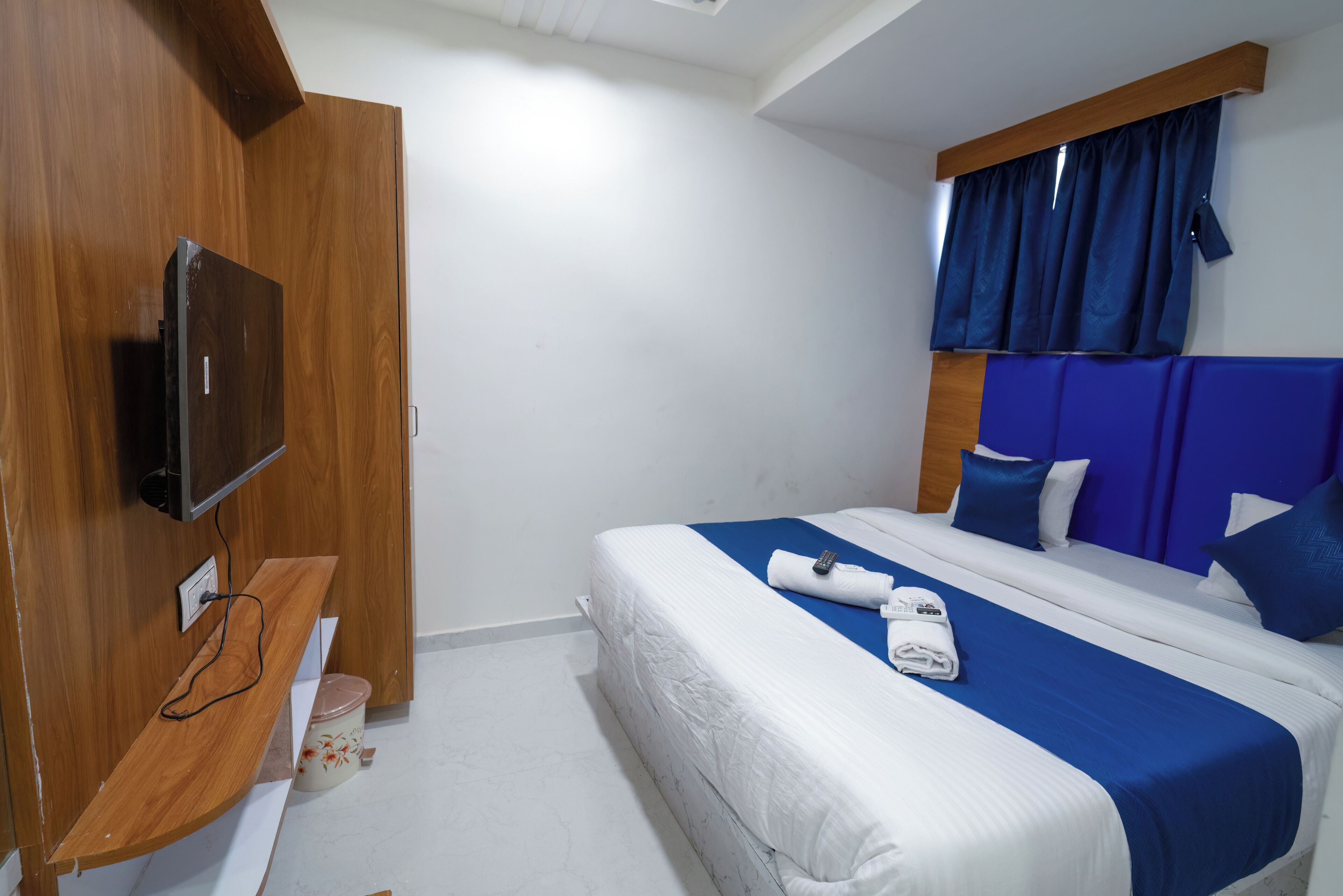 Ein Hotelzimmer mit Bett, Fernseher an einer Holzverkleidung, einem kleinen Tisch und einem Fenster mit Vorhängen.