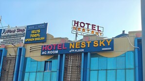 Een gebouw met meerdere borden, waaronder een hotel genaamd 'NEST SKY' op de vierde verdieping, een medische faciliteit 'J P ORTHO CARE' en een opleidingsinstituut 'OMKAR ACADEMY'.