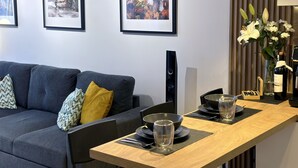 Un salon moderne avec un canapé gris, une table basse en bois et des œuvres d’art encadrées accrochées au mur.